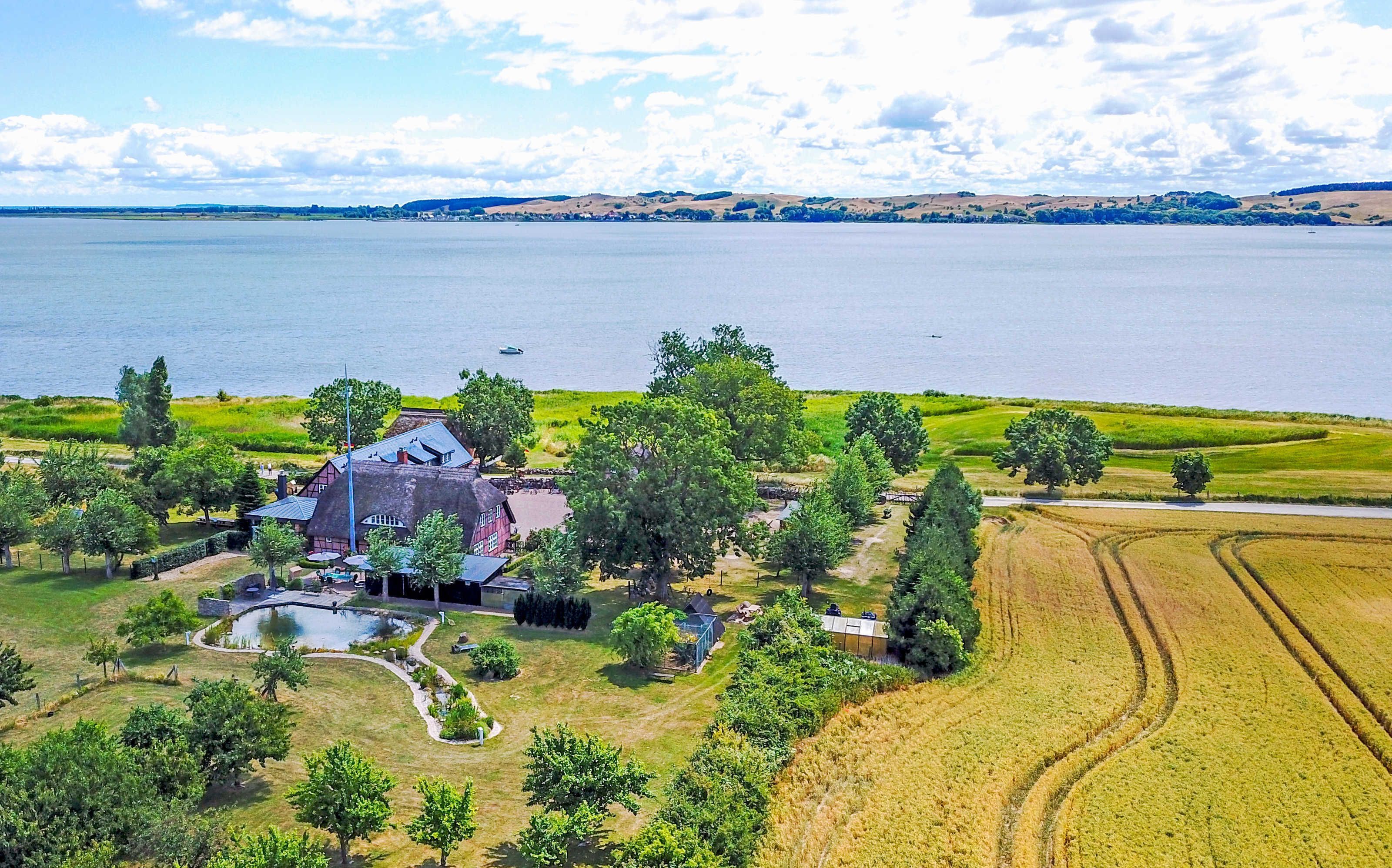 Une grande maison avec un étang, entourée d’arbres et de champs, située près d’un lac.