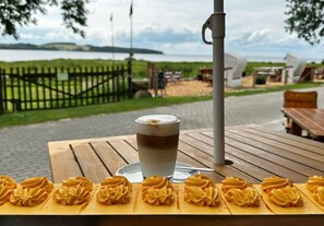 Una mesa con una bebida y pasteles, una valla de madera y vistas a un cuerpo de agua y colinas.