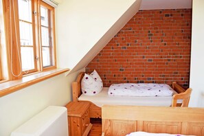 A small, cozy room with a sloped ceiling, a brick wall, a wooden bed, a window with wooden frames, and a white radiator.
