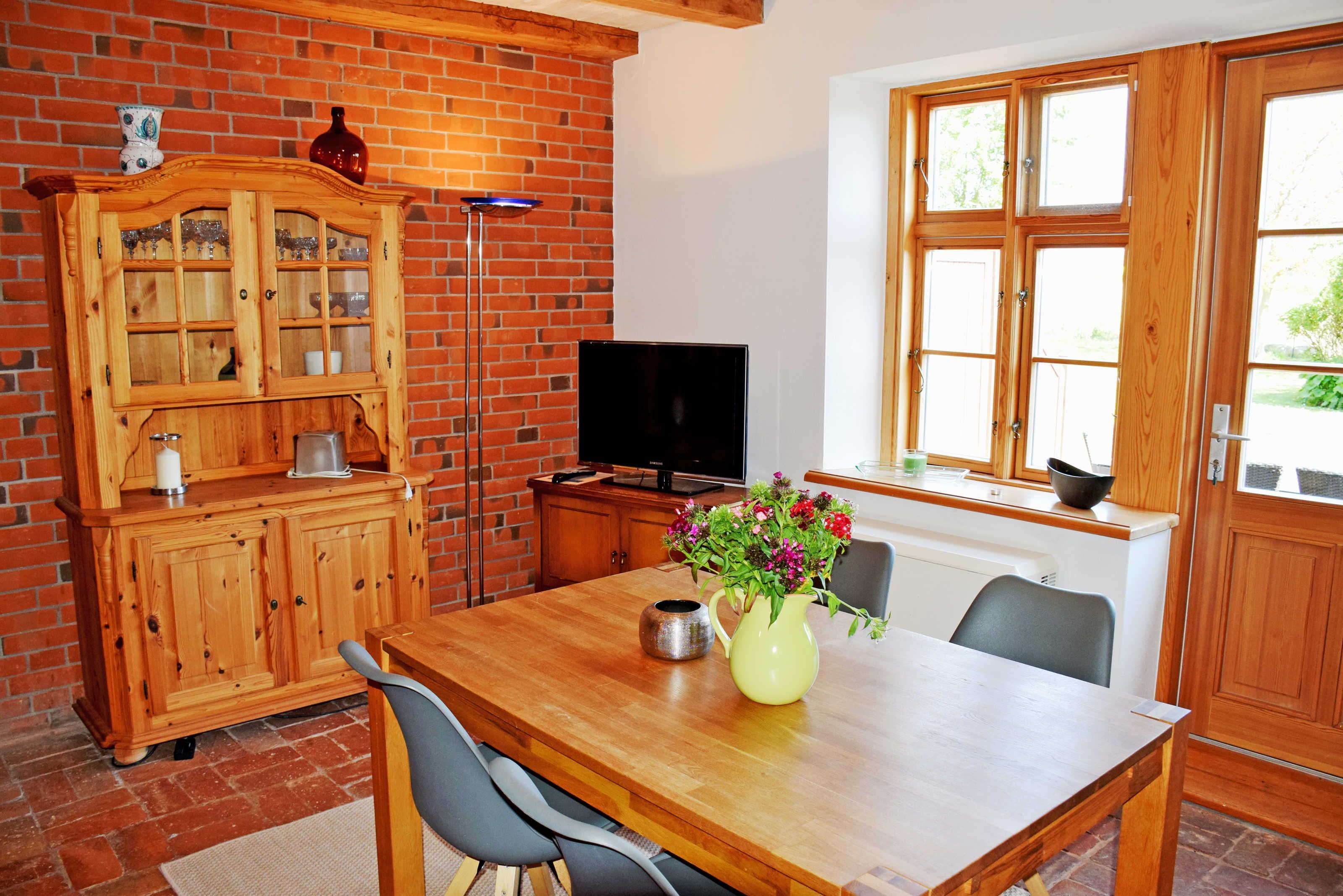Een houten eettafel met stoelen, een televisie, een kast en een raam met houten kozijnen.