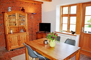 A wooden dining table with chairs, a TV, a cabinet, and a window with wooden frames.