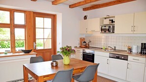 Una cocina moderna con armarios de madera, una mesa de comedor con sillas, un jarrón con flores y una ventana con vistas a zonas verdes.