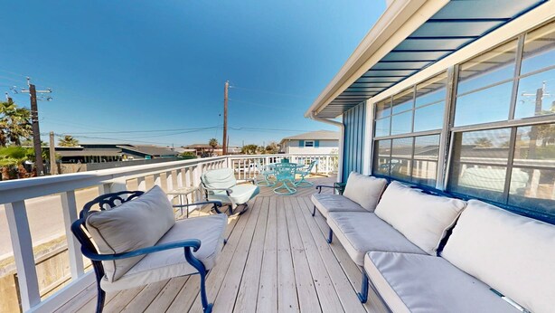 A wooden deck with a white railing, a covered seating area with cushions, and a view of the surrounding area. - Pet Friendly with Large Fenced Yard, Golf Cart Access (Port Aransas)