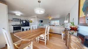 A modern kitchen with white cabinets, a wooden dining table, and a white sofa. - Pet Friendly with Large Fenced Yard, Golf Cart Access (Port Aransas)