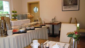 A breakfast buffet setup with various food items and a dining table set for two with utensils and cups. - Double room 5 - PENSION Delia Will in Ahlbeck (Heringsdorf)