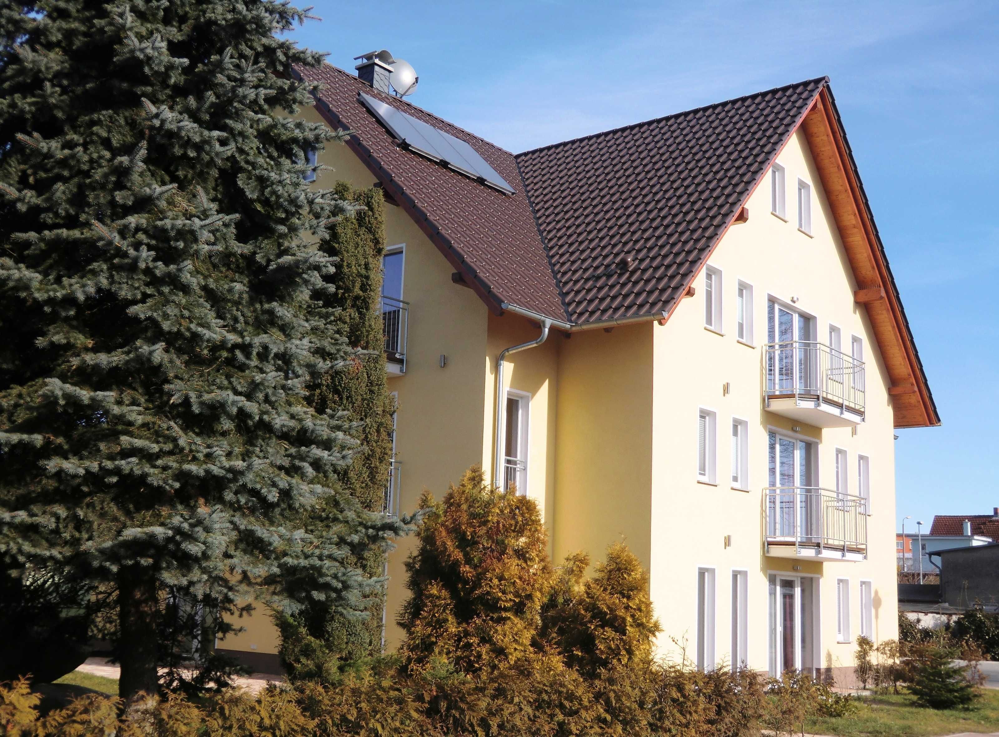 Ein zweistöckiges Gebäude mit einem geneigten Dach, Solaranlagen und einem Balkon.
