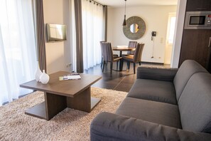 A modern living room with a sofa, a coffee table, and a dining area with chairs and a table.