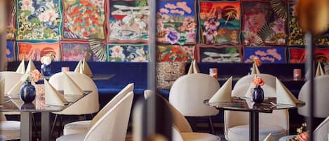 Interior de un restaurante con mesas, sillas y un llamativo mural colorido.