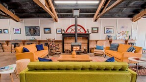 A cozy living room with a fireplace, orange sofas, a green armchair, and wooden beams on the ceiling. - Evergreen (Waldport)
