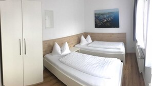 A bedroom with two single beds, a wardrobe, a painting, and a window. - Apartment 2 (2 rooms) - Meutzner Trassenheide, Villa Seute Deern (Trassenheide)