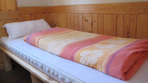 Un letto singolo con testiera in legno e cuscino bianco.