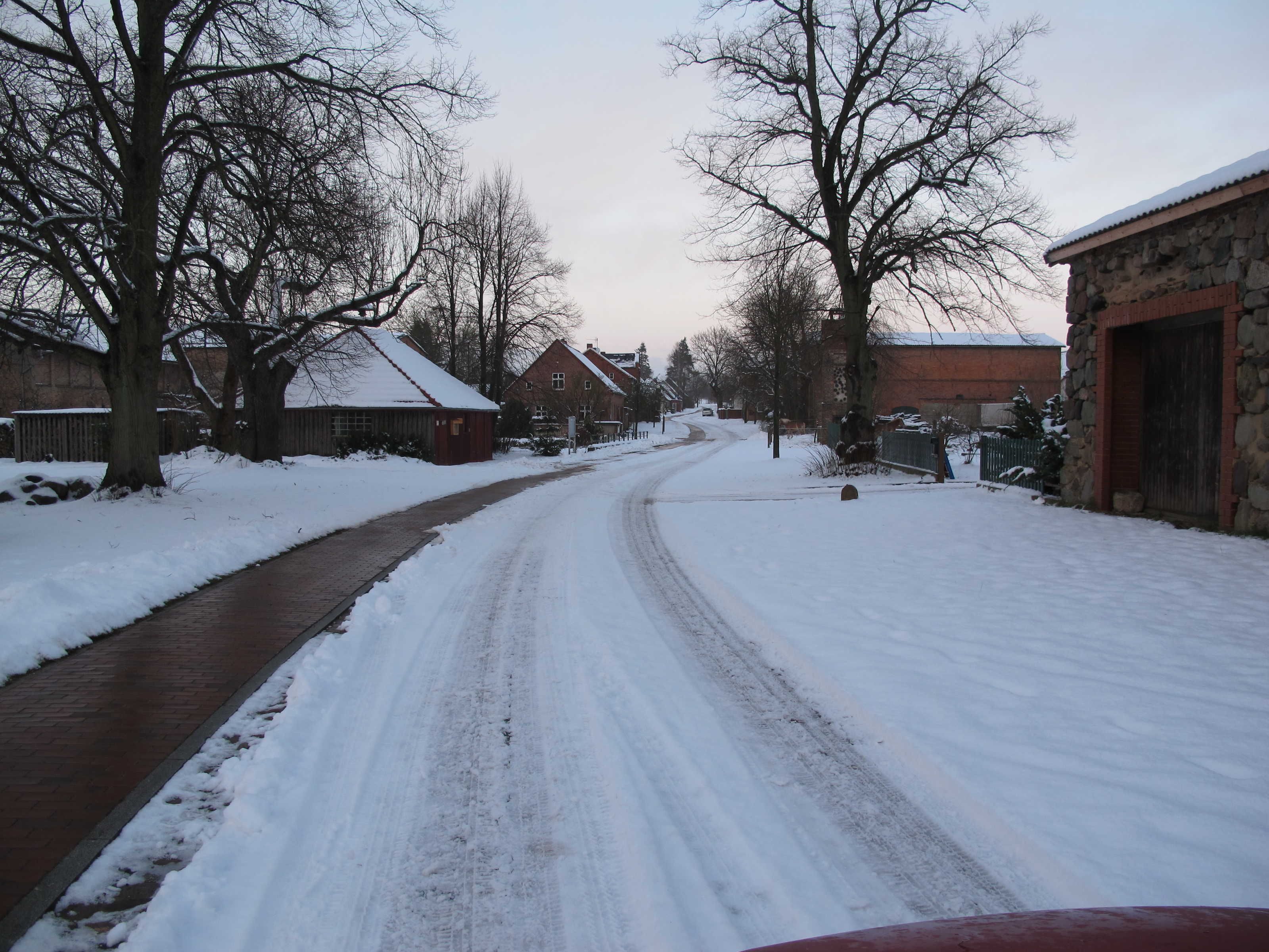 A snow-covered rural road with houses on either side.