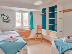 Un dormitorio con dos camas, una silla de madera, una ventana con cortinas y un armario empotrado con estantes.