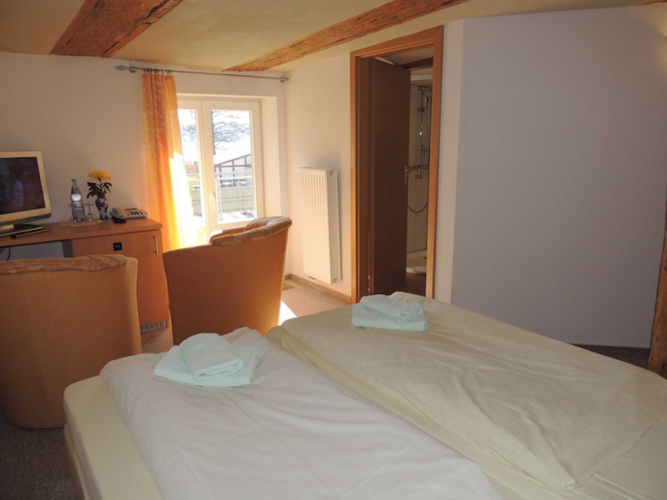 A hotel room with a bed, a desk with a computer, a chair, and a bathroom visible through an open door.