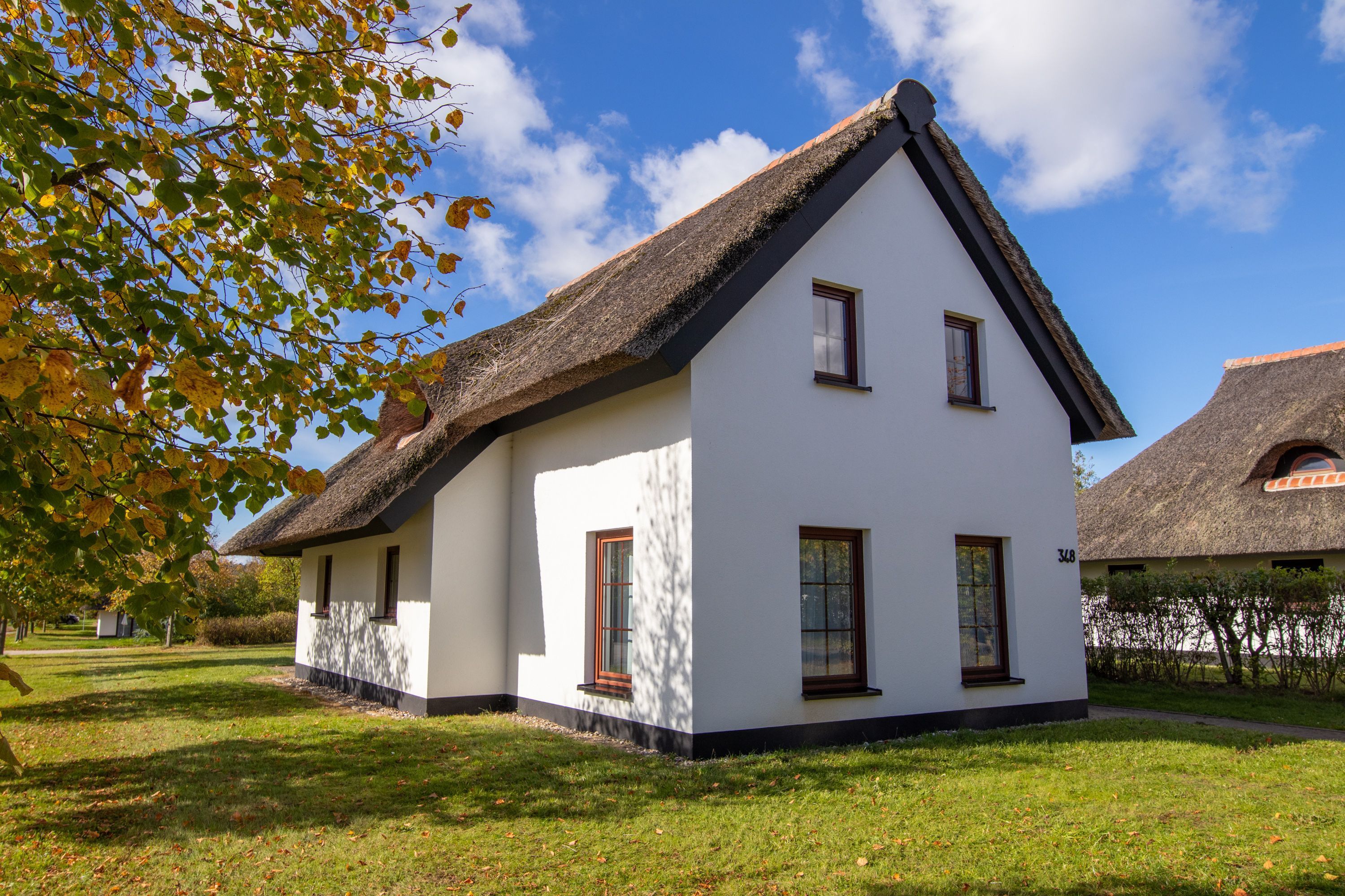 Een wit gebouw met rieten dak, een klein raam en het nummer '348' aan de zijkant.