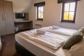 A bedroom with two beds, a TV, a desk, and a window.