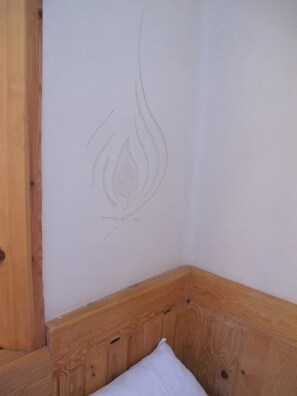 A corner of a room with a wooden headboard and a wall with a faint, abstract design. - Single room Don Bosco - House Lehmkloster am Wangeliner Garten with 5 single rooms (Buchberg)