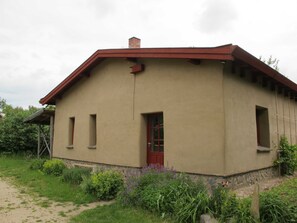 En envåningsbyggnad med ett rött tak, en liten veranda och en dörr.