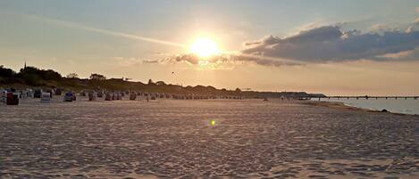 A beach with a sunset, a pier, and beach huts.