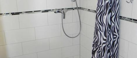 Une salle de bain avec des murs recouverts de carreaux blancs, un rideau de douche à motifs zébrés et un sol carrelé en noir et blanc.