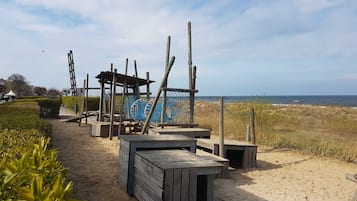 A sandy beach area with wooden structures, including a wooden shelter and a netted play area.