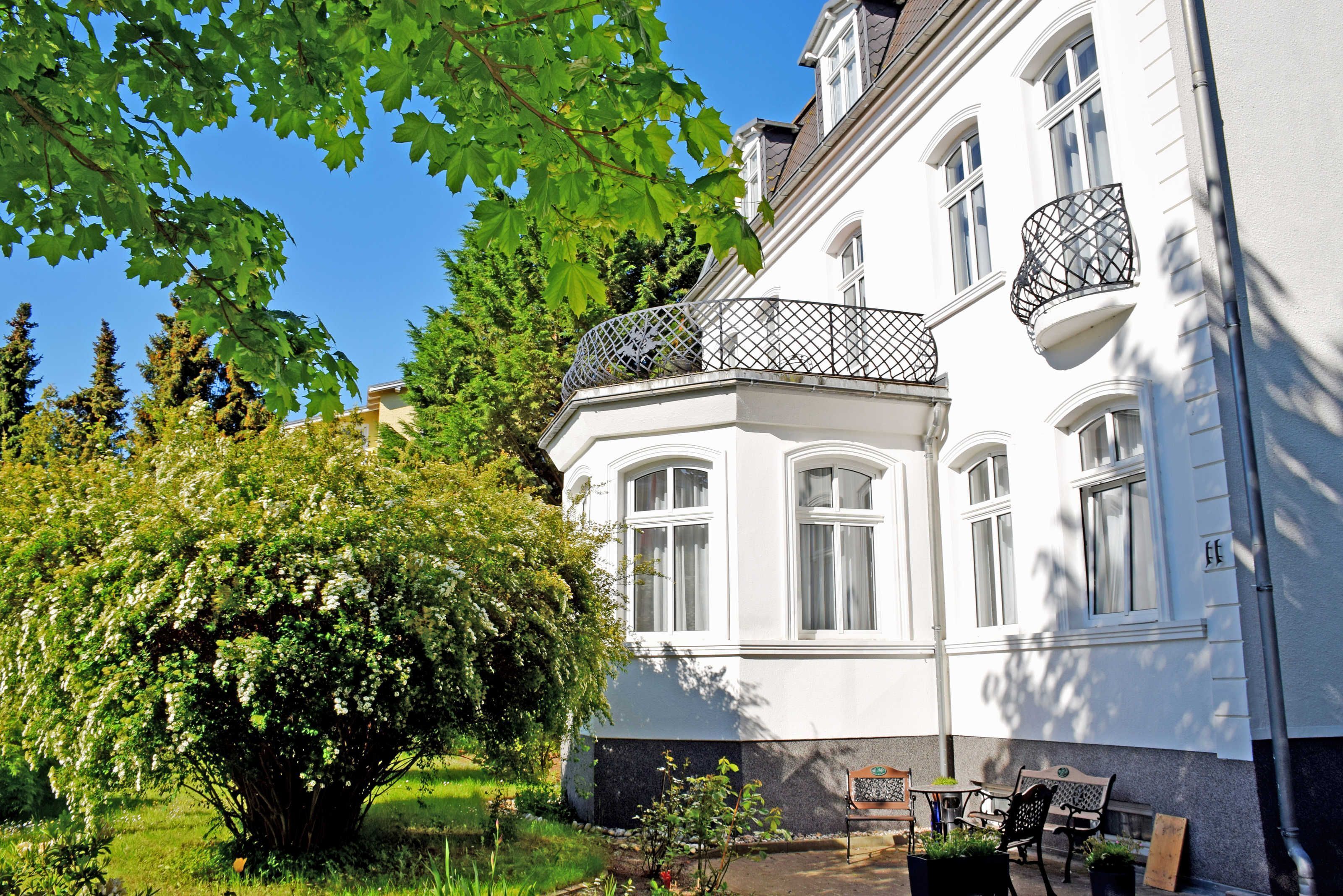 Ein weißes Gebäude mit Balkon und einem Baum im Vordergrund.