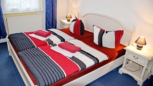 A neatly made bed with striped bedding and red accents, a bedside table with a lamp, and a window with curtains. - 05 Single room - Villa in the Ostseebad Baabe (Baabe)