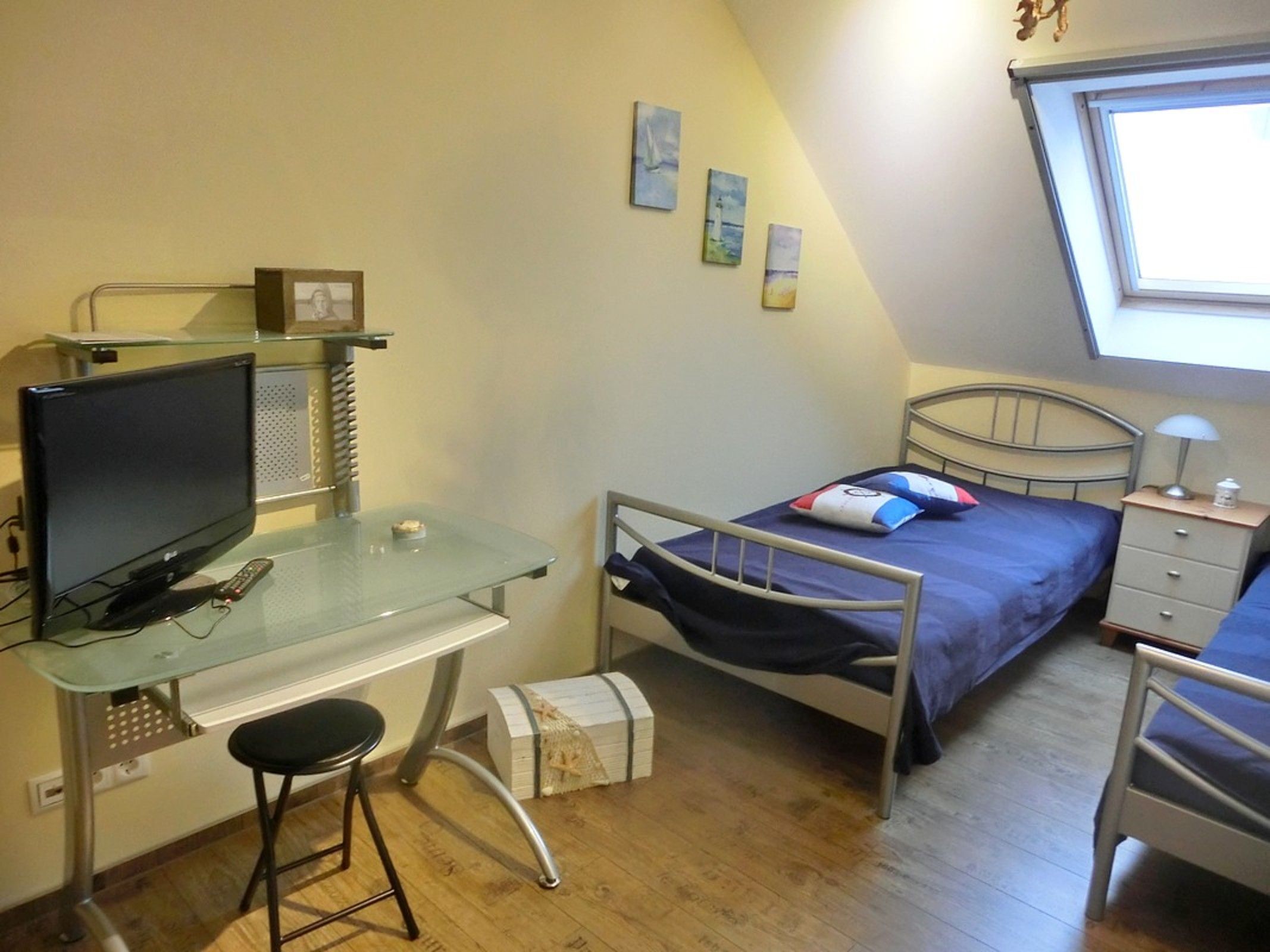 Et hyggeligt, lille værelse med seng, skrivebord med computer, stol, sengebord og et vindue.