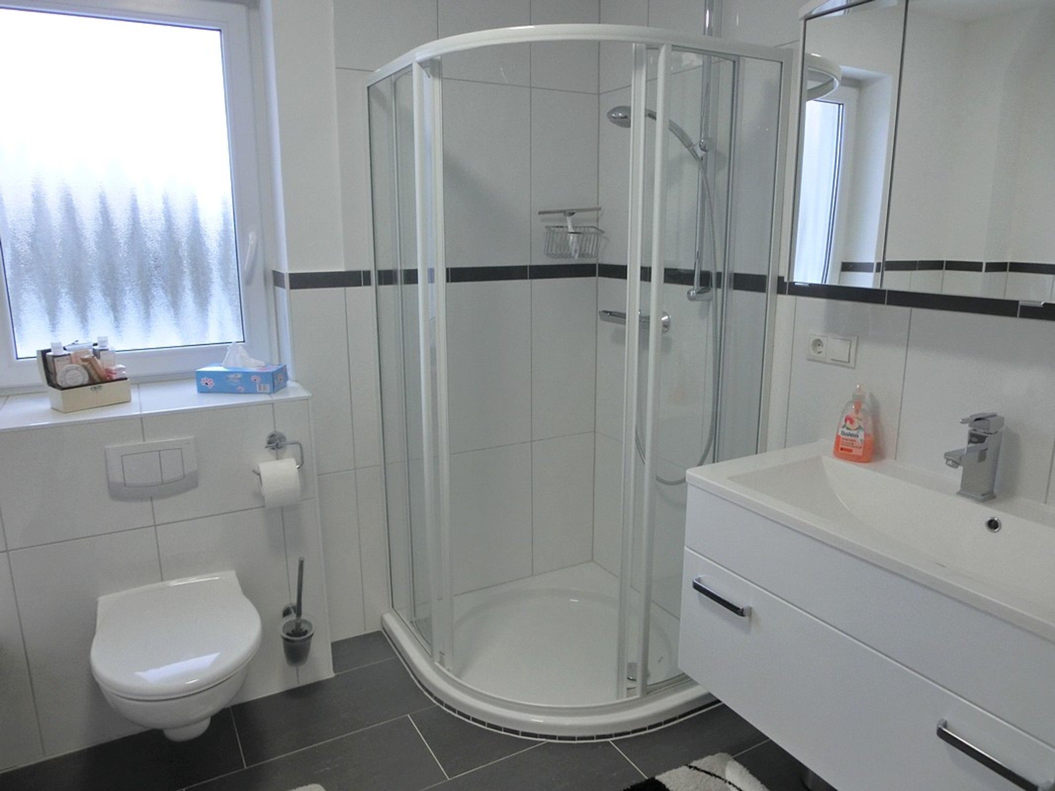 Un baño moderno con ducha envuelta en vidrio, inodoro blanco y lavamanos con dispensador de jabón.