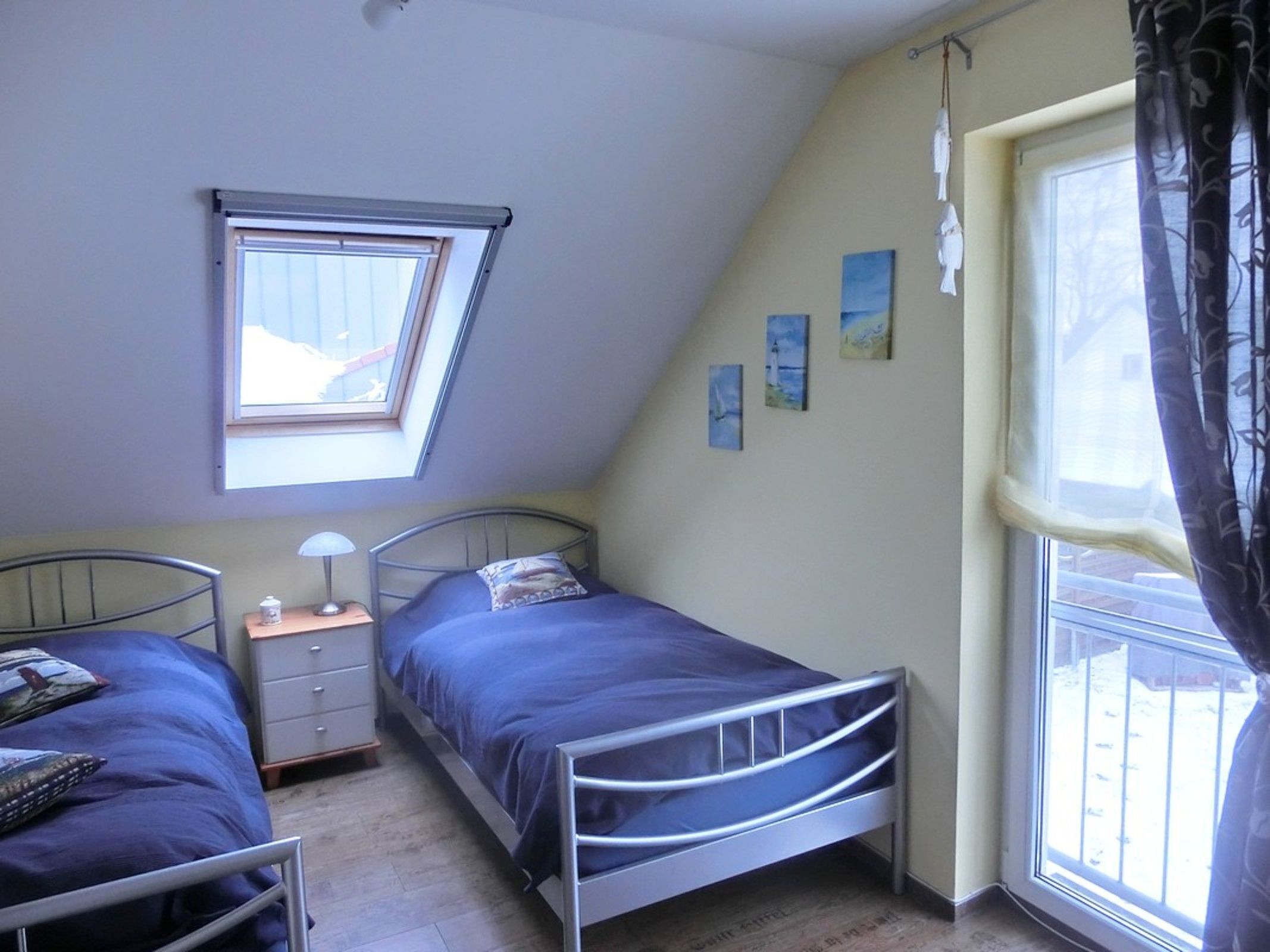 Une chambre avec deux lits, un puits de lumière, une fenêtre avec des rideaux et une table de chevet avec une lampe.