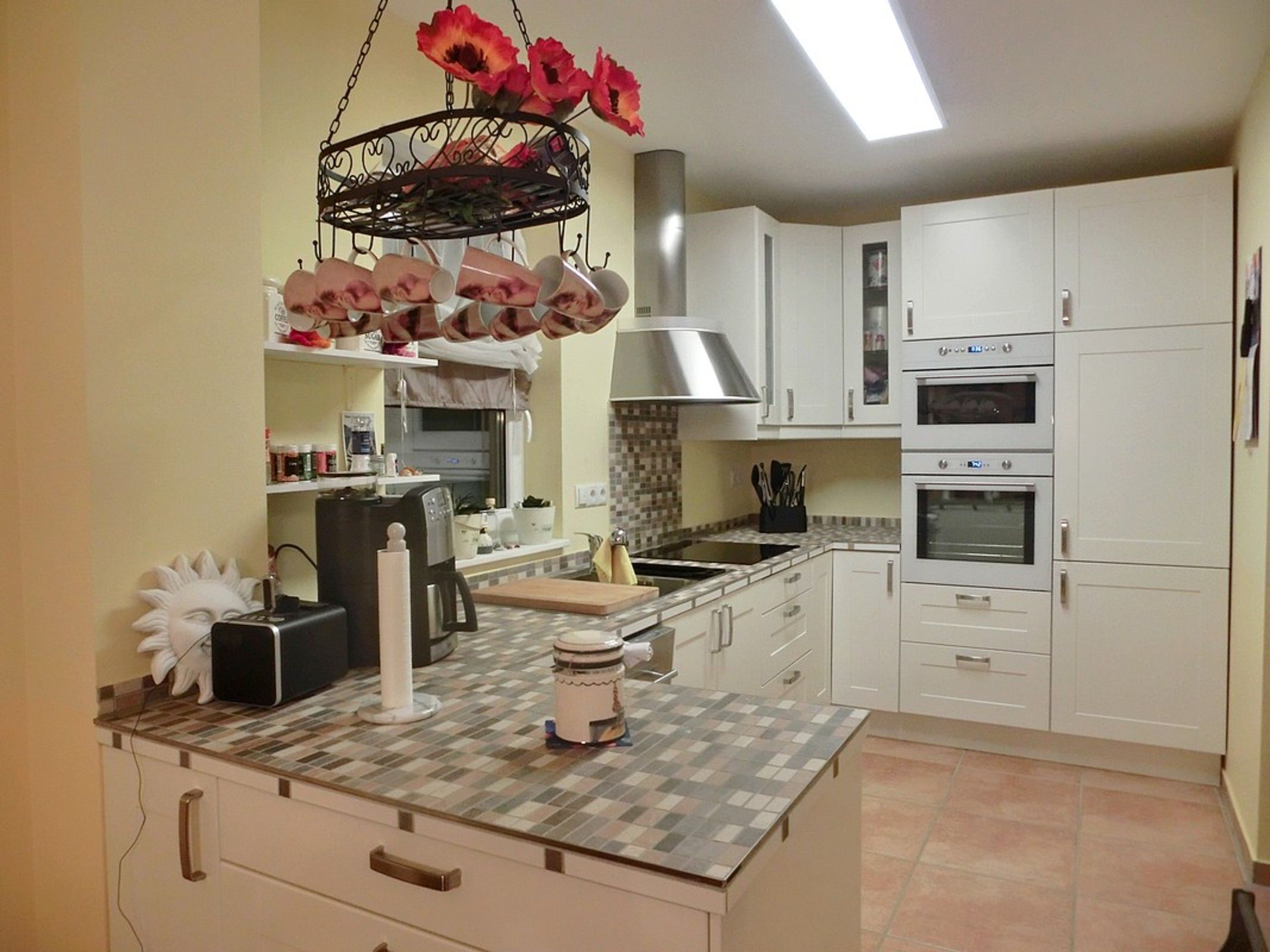 A modern kitchen with white cabinets, a central island, a hanging flower arrangement, and a built-in oven.