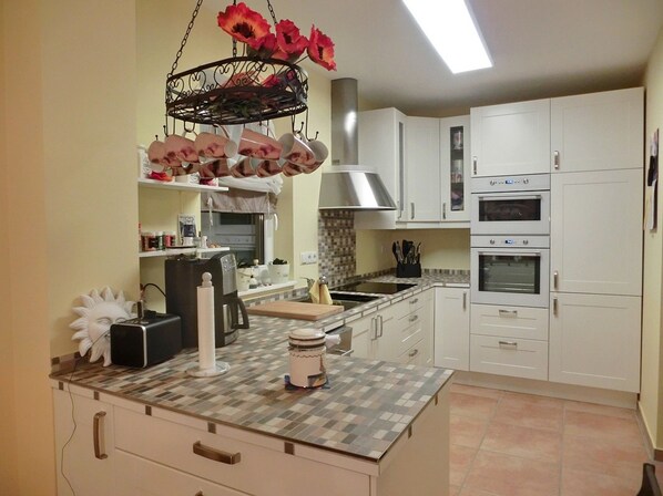 A modern kitchen with white cabinets, a central island, a hanging flower arrangement, and a built-in oven.