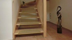 Una escalera de madera con barandilla, un pequeño pájaro decorativo en la pared y una escultura negra en el suelo.