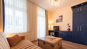 Een hotelkamer met een bank, een houten kist, een televisie, een lamp en een garderobe.