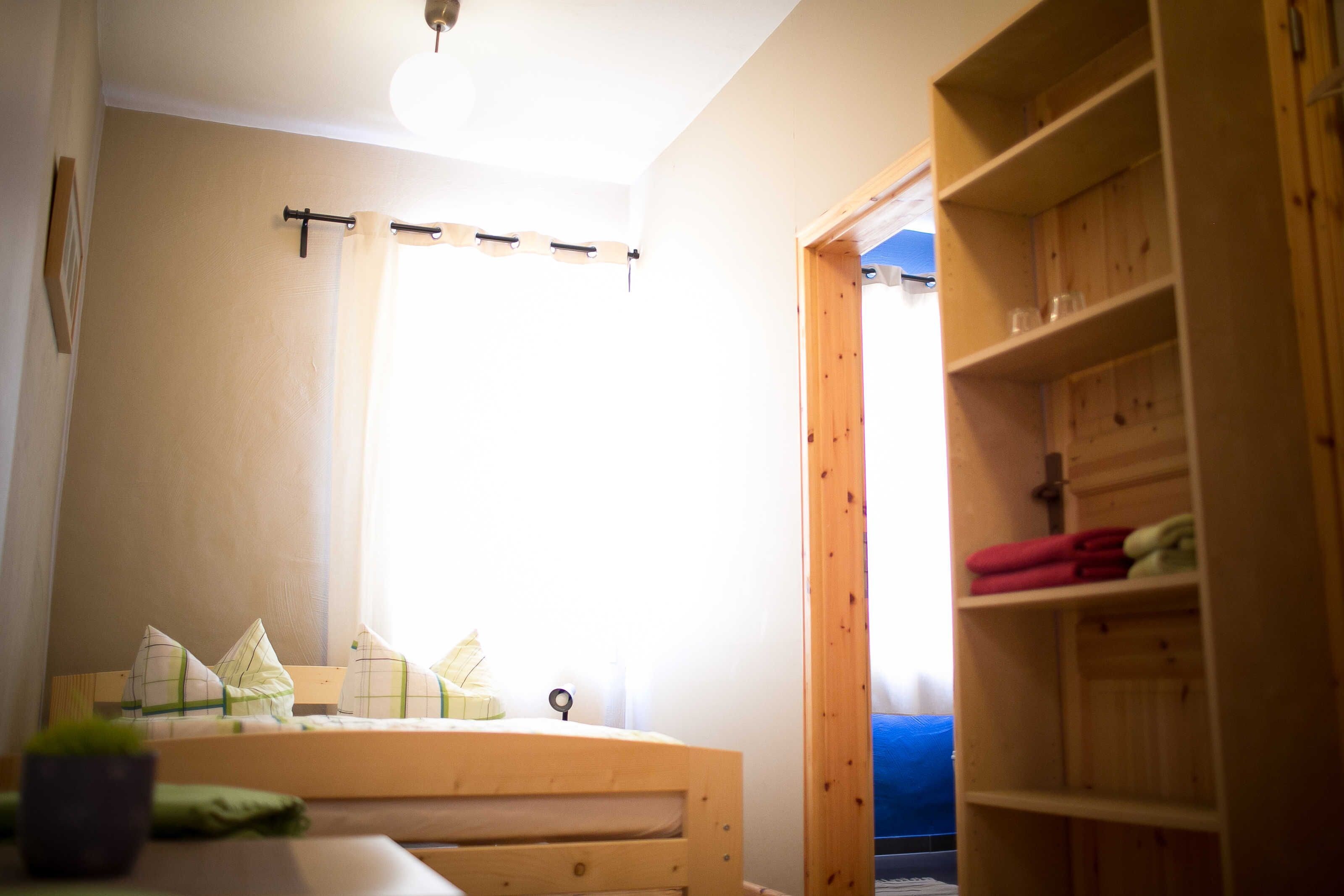 A room with a bed, a wooden shelf, and a window with curtains.