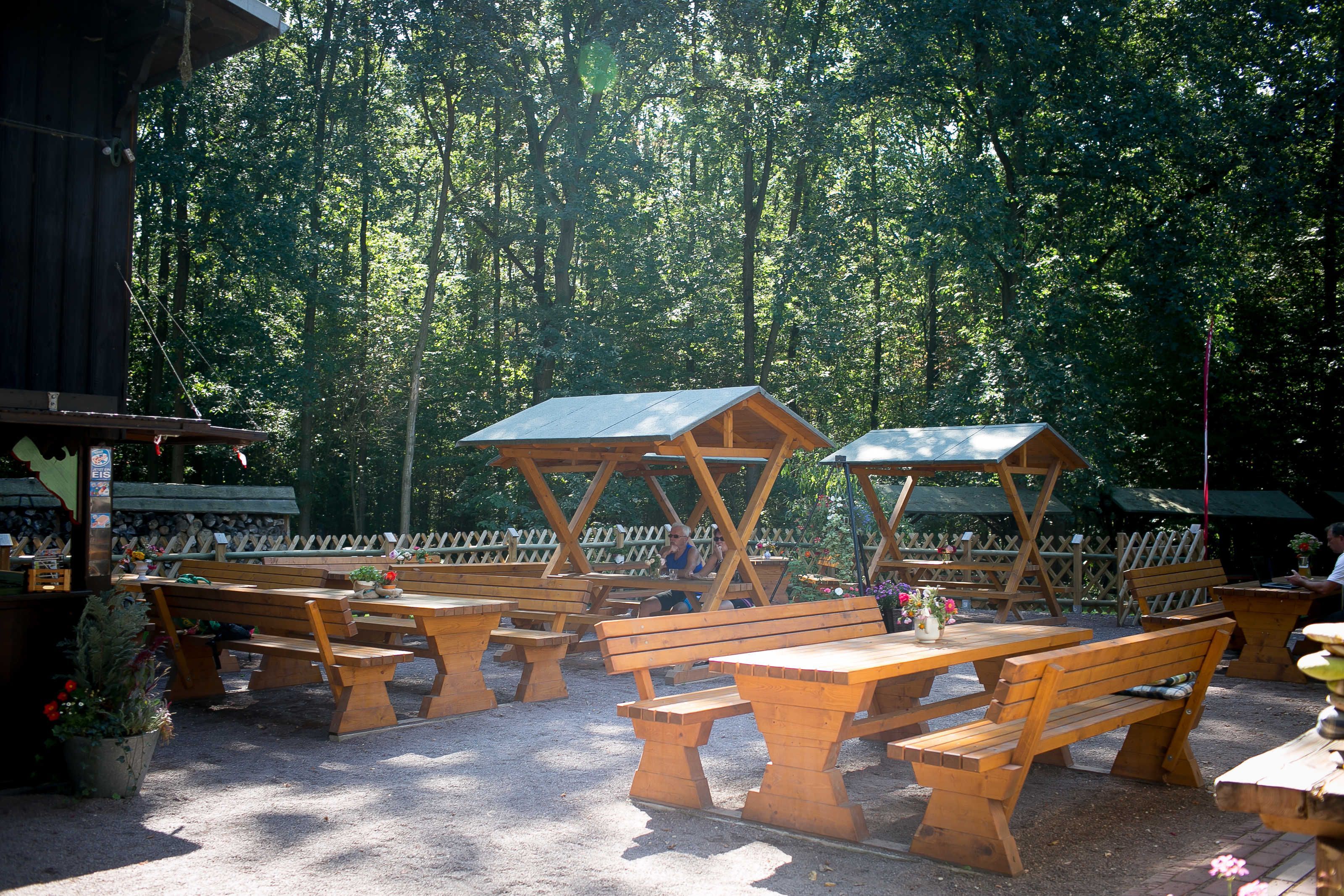 Un espace pique-nique aménagé avec des bancs et des tables en bois, entouré d’une clôture en bois et d’arbres.