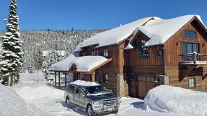 A wooden lodge with a snow-covered roof, a garage, and a parked SUV. - Ski Heaven,  Ski in, Ski out Big Sky Mtn Village Home with Hot Tub (Big Sky)