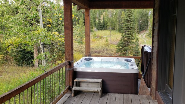 A wooden deck with a hot tub and a wooden bench, overlooking a forested area. - Ski Heaven,  Ski in, Ski out Big Sky Mtn Village Home with Hot Tub (Big Sky)