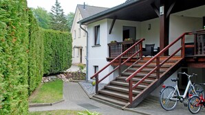 A house with a staircase leading to a porch, a garden with a hedge, and two bicycles parked outside. - House Meeresgeflüster (R) - holiday house Meeresgeflüster (Sellin)