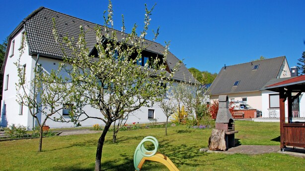 A residential area with a white house, a tree with blossoms, and a playground slide. - House Meeresgeflüster (R) - holiday house Meeresgeflüster (Sellin)