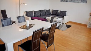 A modern living room with a white sofa, grey cushions, a white coffee table, and a dining table with chairs. - House Meeresgeflüster (R) - holiday house Meeresgeflüster (Sellin)