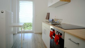 Une cuisine moderne dotée d’un four encastré, d’un plan de travail avec une bouilloire et d’une fenêtre avec des stores.