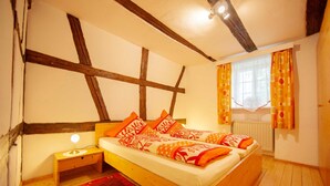 Quarto com cama de madeira, mesa de cabeceira, tapete vermelho e janela com cortinas.