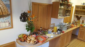 Uma bancada de cozinha com diversos itens de pequeno-almoço, incluindo frutas, pastelaria e bebidas.