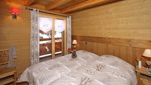 Un dormitorio de cabaña de madera con una cama, dos lámparas de noche, una mesita de noche y una ventana con cortinas.