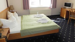 Une chambre d’hôtel équipée d’un lit, d’un bureau, d’une chaise, d’une télévision et d’une fenêtre avec des rideaux.