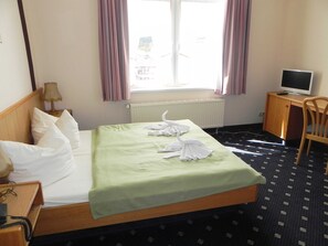 Ein Hotelzimmer mit Bett, Schreibtisch, Stuhl, Fernseher und einem fenster mit Vorhängen.