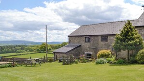 A stone building with a sloped roof, surrounded by a grassy field and a wooden fence. - Mountain View-UK11825 (Sarnau, near Brecon)