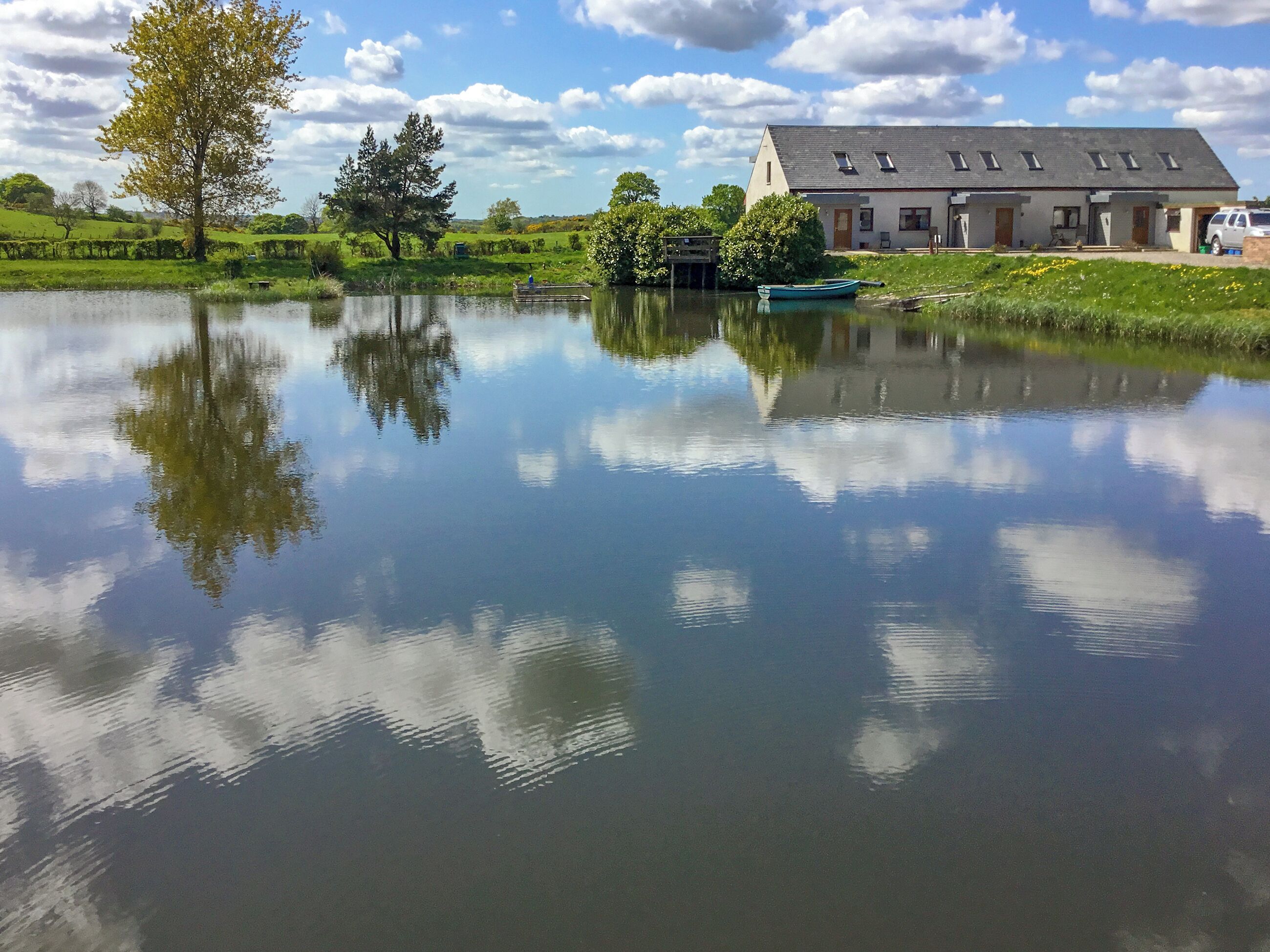 A serene lakeside view with a house featuring a sloped roof and multiple windows.