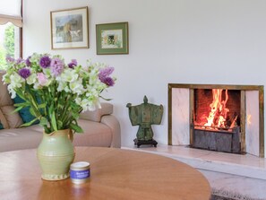 A living room with a sofa, a vase of flowers, a small statue, and a fireplace with a fire.